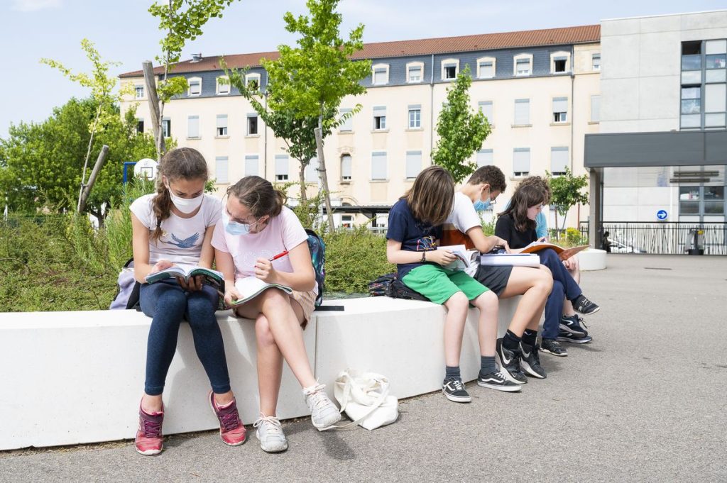collégiens assis sur un banc en béton, par binome, étudiant un livre