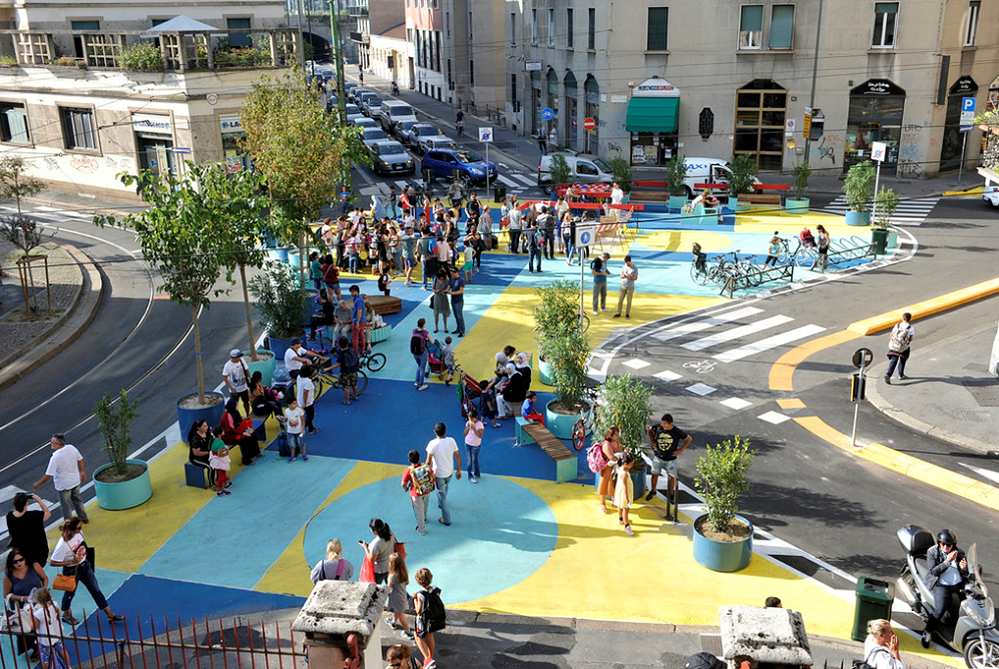 Une foule de gens se déplace sur une rue animée et colorée avec des formes bleues et jaunes.