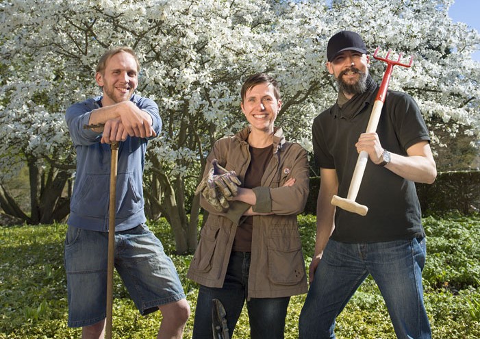 Trois adultes souriant à la caméra et tenant des outils de jardinage. En arrière plan, un arbre en fleurs