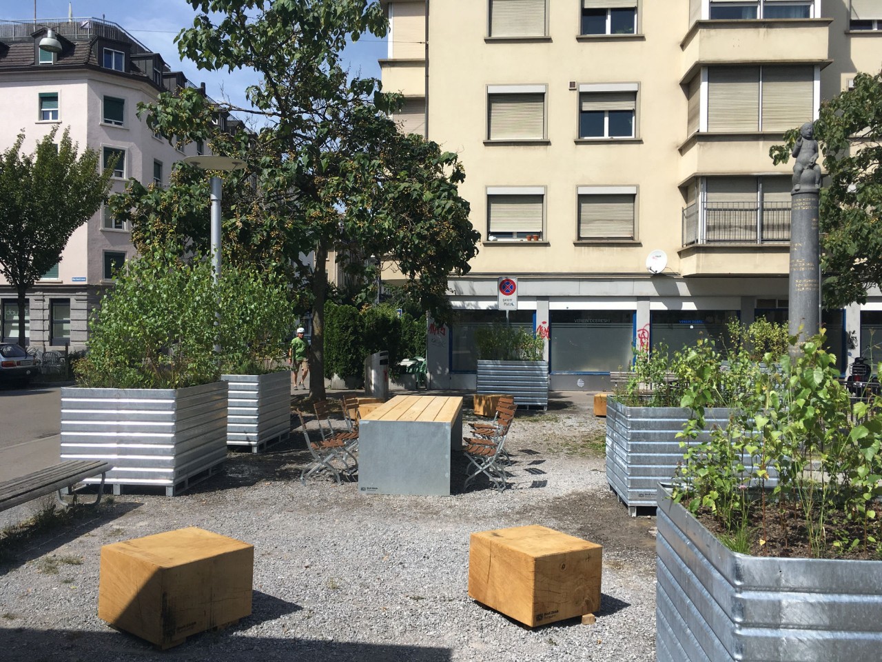 La photo montre du mobilier urbain (table, chaises, cubes en bois...) implanté de façon éphémère à Zurich.