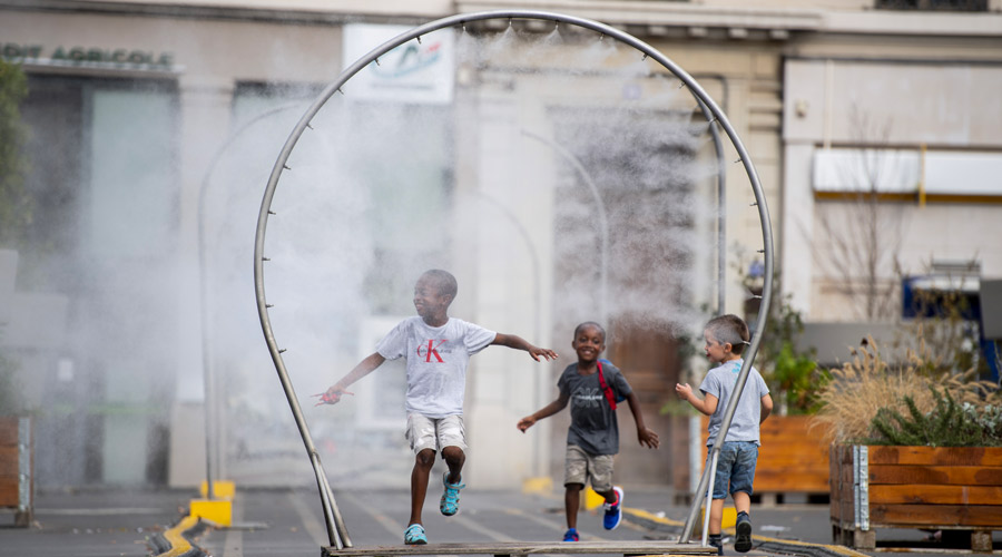 Jeunes enfants qui jouent dans la rue sous des brumisateurs installés temporairement