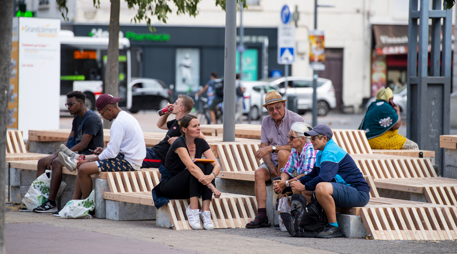 Adultes qui discutent sur des bancs en bois et en béton qui forment une sorte d'escalier. Ces assises sont situées sur la place GrandClément à Villeurbanne