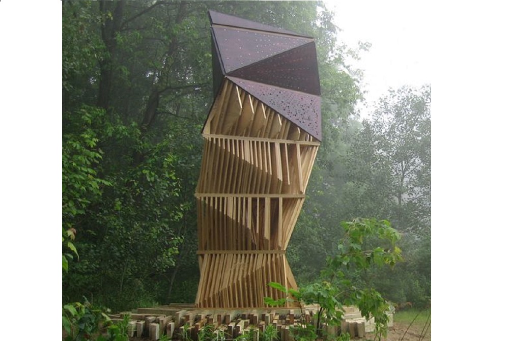 Une sculpture en bois en forme de tour, au milieu d'une forêt, dont l'objectif est de devenir un nid à chauve souris.