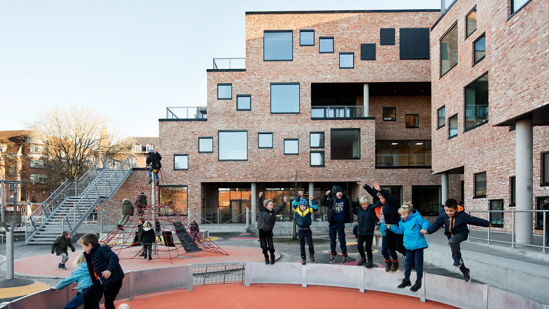 Enfants dans une cour d'école pris en photo en plein saut, avec l'école en arrière-plan